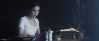 Movie still from “Carmilla” (2019), directed by Emily Harris – A woman sitting at a table in front of a cup; Medium shot, Over the shoulder angle