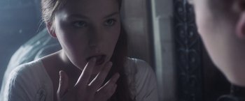 Movie still from “Carmilla” (2019), directed by Emily Harris – A woman with blue eyes and dark hair is holding her hand to her mouth; Close Up shot, Over the shoulder angle