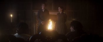 Movie still from “Carmilla” (2019), directed by Emily Harris – A man and a woman standing in front of a candle; Wide shot, Over the shoulder angle