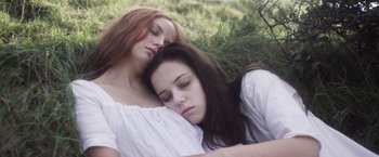 Movie still from “Carmilla” (2019), directed by Emily Harris – Two young women sleeping on the ground in a field; Close Up shot, Overhead angle