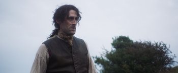 Movie still from “Carmilla” (2019), directed by Emily Harris – A man with long black hair wearing a vest; Medium shot, Low angle