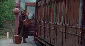 Movie still from “Carrington” (1995), directed by Christopher Hampton – A man holding an umbrella standing in front of a train; Wide shot, High angle