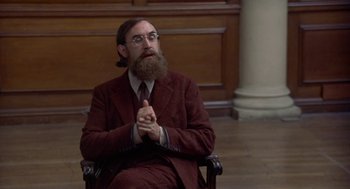 Movie still from “Carrington” (1995), directed by Christopher Hampton – A man in a suit and beard sitting in a chair; Medium shot, Over the shoulder angle