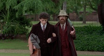 Movie still from “Carrington” (1995), directed by Christopher Hampton – Two men walking in a park wearing suits and hats; Medium shot, Over the shoulder angle