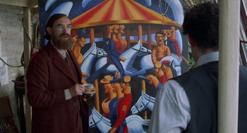 Movie still from “Carrington” (1995), directed by Christopher Hampton – A man standing in front of a painting of a merry go round; Medium shot, Over the shoulder angle