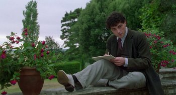 Movie still from “Carrington” (1995), directed by Christopher Hampton – A man sitting on the ground writing on a piece of paper; Medium shot, Low angle