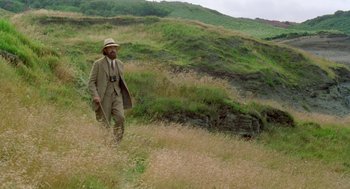 Movie still from “Carrington” (1995), directed by Christopher Hampton – A man in a suit and hat walking through a field; Wide shot, High angle