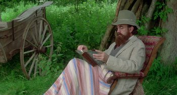 Movie still from “Carrington” (1995), directed by Christopher Hampton – A man sitting in a chair holding a book; Medium shot, High angle