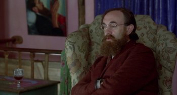 Movie still from “Carrington” (1995), directed by Christopher Hampton – A man sitting in a chair with his arms crossed; Medium shot, Low angle