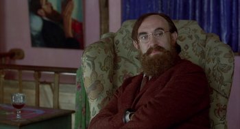 Movie still from “Carrington” (1995), directed by Christopher Hampton – A man sitting in a chair with his arms crossed; Close Up shot, Over the shoulder angle
