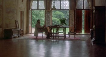Movie still from “Carrington” (1995), directed by Christopher Hampton – A man sitting at a table in front of a large window; Wide shot, High angle