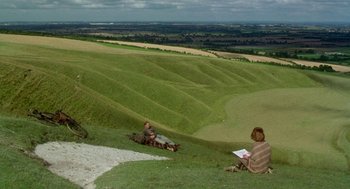 Movie still from “Carrington” (1995), directed by Christopher Hampton – Two people sitting on a grassy hill looking at a book; Extreme Wide shot, High angle
