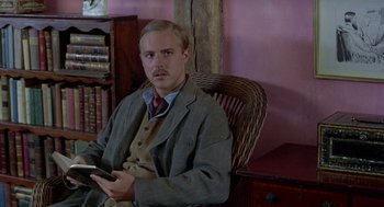 Movie still from “Carrington” (1995), directed by Christopher Hampton – A man sitting in a chair holding a cell phone; Medium shot, Low angle