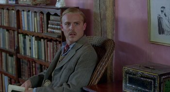 Movie still from “Carrington” (1995), directed by Christopher Hampton – A man sitting in a chair in front of a bookshelf; Medium shot, Low angle