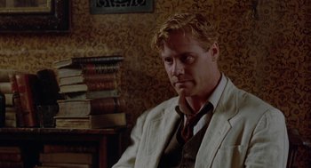 Movie still from “Carrington” (1995), directed by Christopher Hampton – A man sitting in front of a stack of books; Medium shot, Over the shoulder angle