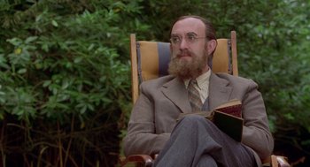 Movie still from “Carrington” (1995), directed by Christopher Hampton – A man sitting in a chair with a book in his lap; Medium shot, Over the shoulder angle