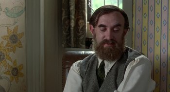 Movie still from “Carrington” (1995), directed by Christopher Hampton – A man sitting in a chair wearing a tie and a vest; Close Up shot, Over the shoulder angle