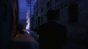 Movie still from “Cast a Deadly Spell” (1991), directed by Martin Campbell – A man wearing a hat and a suit standing on the side of the street; Extreme Wide shot, Over the shoulder angle