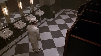 Movie still from “Cast a Deadly Spell” (1991), directed by Martin Campbell – A man in a white suit and white hat standing in front of a mirror in a bathroom; Wide shot, High angle