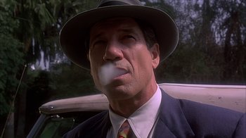 Movie still from “Cast a Deadly Spell” (1991), directed by Martin Campbell – A man in a suit and hat smoking a cigarette; Close Up shot, Low angle