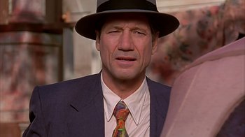 Movie still from “Cast a Deadly Spell” (1991), directed by Martin Campbell – A person wearing a suit and a hat; Close Up shot, Over the shoulder angle