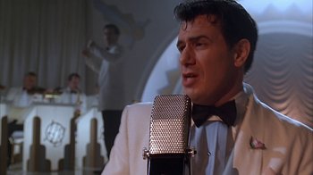 Movie still from “Cast a Deadly Spell” (1991), directed by Martin Campbell – A man in a white suit and bow tie singing into a microphone; Close Up shot, Low angle