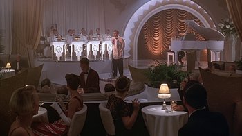 Movie still from “Cast a Deadly Spell” (1991), directed by Martin Campbell – A group of people sitting at tables in front of a microphone; Wide shot, High angle