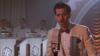Movie still from “Cast a Deadly Spell” (1991), directed by Martin Campbell – A man in a white suit and red bow tie is singing; Medium shot, Low angle
