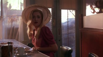 Movie still from “Cast a Deadly Spell” (1991), directed by Martin Campbell – A woman in a hat is sitting at a counter; Medium shot, Over the shoulder angle