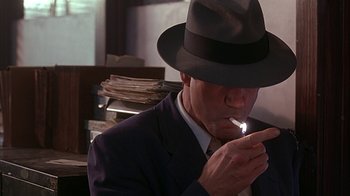 Movie still from “Cast a Deadly Spell” (1991), directed by Martin Campbell – A man in a suit and a hat smoking a cigarette; Close Up shot, Over the shoulder angle