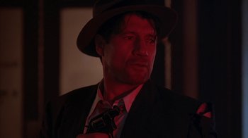 Movie still from “Cast a Deadly Spell” (1991), directed by Martin Campbell – A man in a suit and a hat is holding a camera; Close Up shot, Low angle