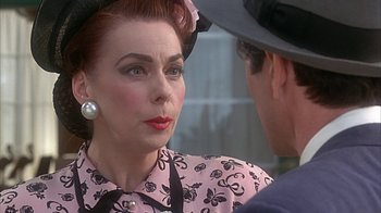 Movie still from “Cast a Deadly Spell” (1991), directed by Martin Campbell – An older woman wearing a pink dress and a hat talking to a younger man; Close Up shot, Over the shoulder angle