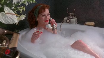 Movie still from “Cast a Deadly Spell” (1991), directed by Martin Campbell – A woman sitting in a bath tub holding a phone and a glass of wine; Medium shot, High angle