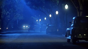 Movie still from “Cast a Deadly Spell” (1991), directed by Martin Campbell – Cars driving down a street at night in the dark; Extreme Wide shot, Low angle