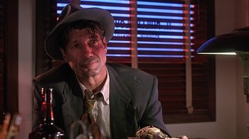 Movie still from “Cast a Deadly Spell” (1991), directed by Martin Campbell – A man in a suit and hat sitting at a dinner table; Close Up shot, Low angle