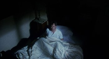 Movie still from “Castle Freak” (1995), directed by Stuart Gordon – A man laying in bed under a blanket; Medium shot, Overhead angle