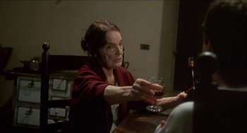 Movie still from “Castle Freak” (1995), directed by Stuart Gordon – An older woman sitting at a table holding a wine glass; Medium shot, Over the shoulder angle