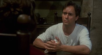 Movie still from “Castle Freak” (1995), directed by Stuart Gordon – A man sitting at a table holding a nintendo wii game controller; Close Up shot, Over the shoulder angle