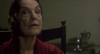 Movie still from “Castle Freak” (1995), directed by Stuart Gordon – An older woman looking at the camera in a dark room; Close Up shot, Low angle