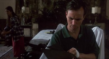 Movie still from “Castle Freak” (1995), directed by Stuart Gordon – A man sitting at a table looking down at a piece of paper; Close Up shot, Low angle