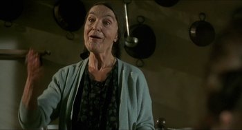 Movie still from “Castle Freak” (1995), directed by Stuart Gordon – An older woman is smiling in front of pots; Close Up shot, Low angle