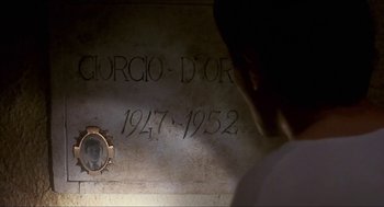 Movie still from “Castle Freak” (1995), directed by Stuart Gordon – A man is looking at a plaque in a cemetery; Extreme Close Up shot, Over the shoulder angle