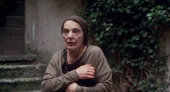 Movie still from “Castle Freak” (1995), directed by Stuart Gordon – An older woman with a head scarf is sitting outside; Close Up shot, Low angle