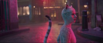Movie still from “Cats” (2019), directed by Tom Hooper – A white cat standing in the middle of a street; Medium shot, Over the shoulder angle