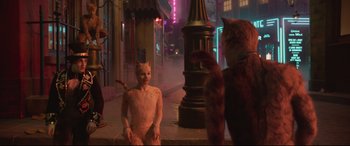 Movie still from “Cats” (2019), directed by Tom Hooper – Two cats and a person sitting on the sidewalk; Wide shot, Over the shoulder angle