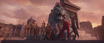Movie still from “Cats” (2019), directed by Tom Hooper – A group of people standing next to a statue of a lion; Wide shot, Low angle