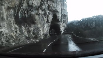 Movie still from “Cave of Forgotten Dreams” (2010), directed by Werner Herzog – A car driving down a road next to a rock wall; Extreme Wide shot, High angle
