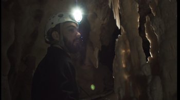 Movie still from “Cave of Forgotten Dreams” (2010), directed by Werner Herzog – A man wearing a helmet and a jacket in a cave; Medium shot, Low angle