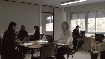 Movie still from “Cave of Forgotten Dreams” (2010), directed by Werner Herzog – An older woman sitting in front of a laptop computer; Wide shot, High angle