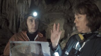 Movie still from “Cave of Forgotten Dreams” (2010), directed by Werner Herzog – Two people are talking in a cave with a flashlight on their head; Medium shot, Over the shoulder angle